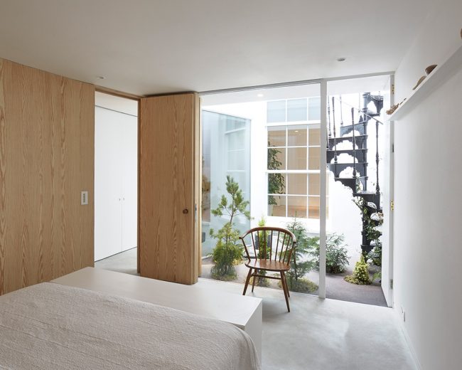 Minimal bedroom with frameless glass wall looking out into a small plant filled courtyard