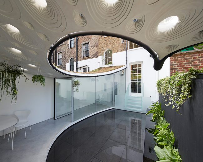 Paved garden terrace with curved glass walls and a glass staircase