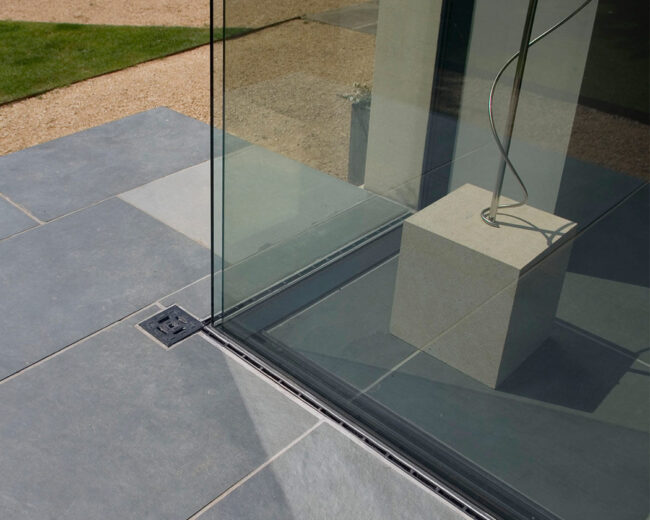 Frameless corner glazing set into a stone patio