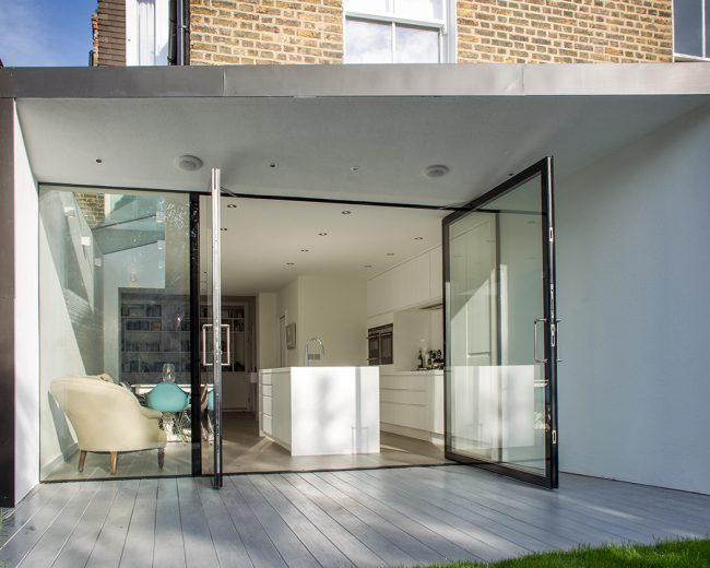 Metal-framed kitchen extension with frameless glass walls and pivot doors