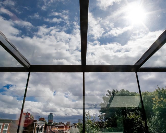 Sun streaming through a frameless glass extension with an open sliding rooflight