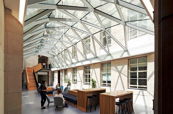 People working in an open-plan atrium office with a framed glass roof