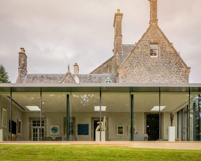 Glazed box extension on a historic country house featuring fixed frameless glass and Sky-Frame sliding doors