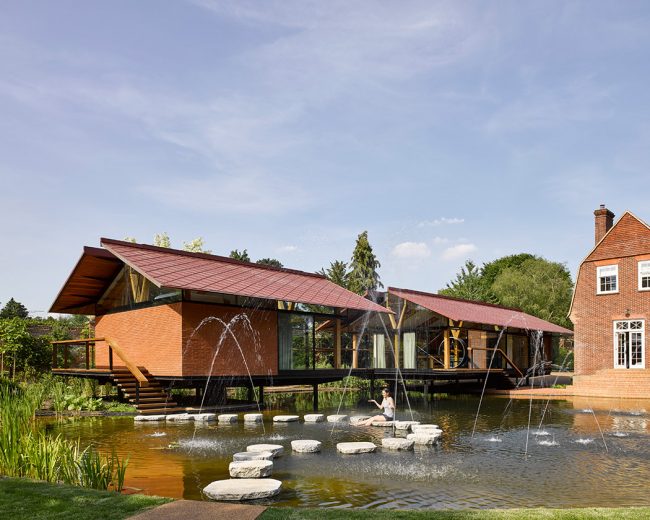Outbuilding on stilts above a large pond featuring glass roofs, glass walls and sliding glass doors
